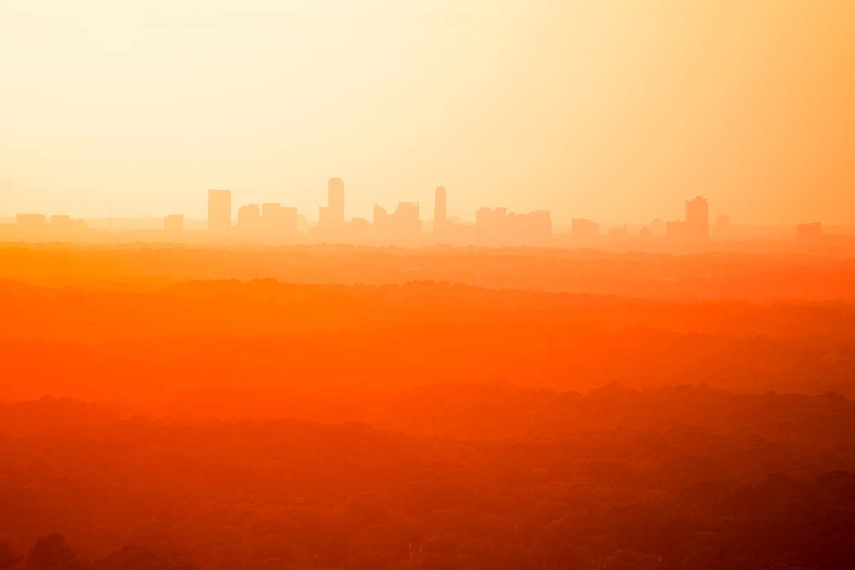 Die Silhouette einer Skyline bei Sonnenuntergang, wobei orangefarbene und rote Farbtöne die Landschaft in ein warmes Licht tauchen.