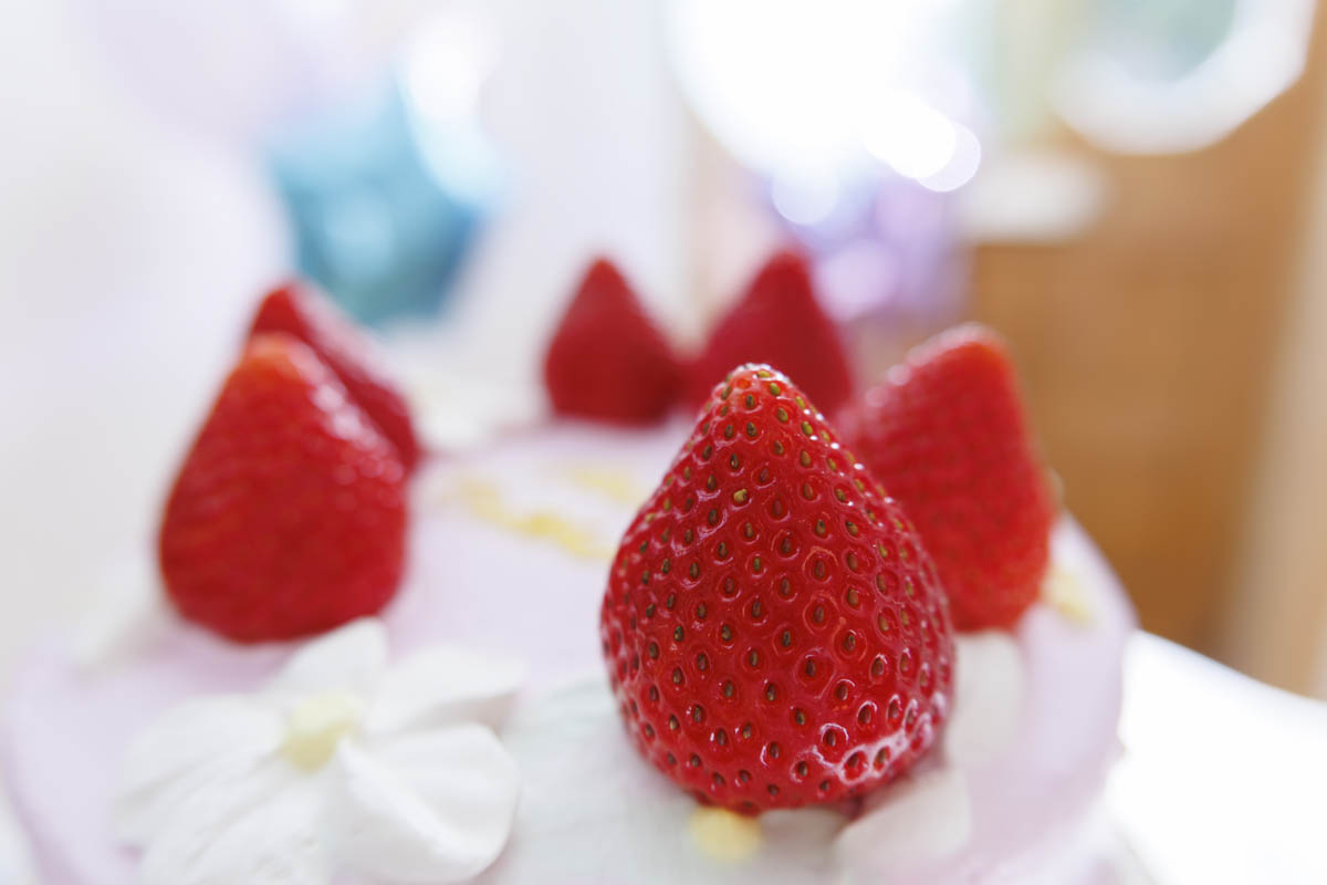 Close-up of a pink cake topped with fresh strawberries and decorative white flowers.
