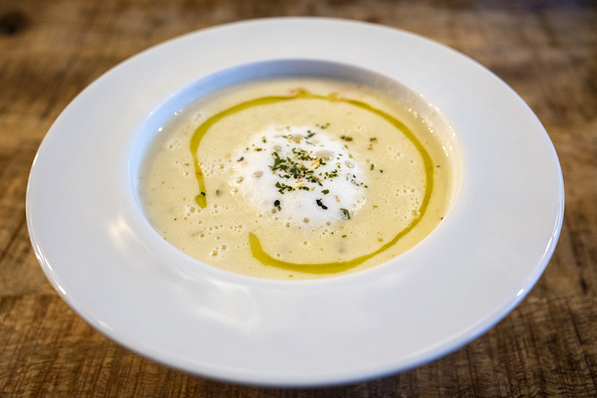 Eine Schüssel cremige Suppe, garniert mit einem Spritzer Olivenöl und Kräutern, serviert auf einem weißen Teller vor dem Hintergrund eines Holztisches.