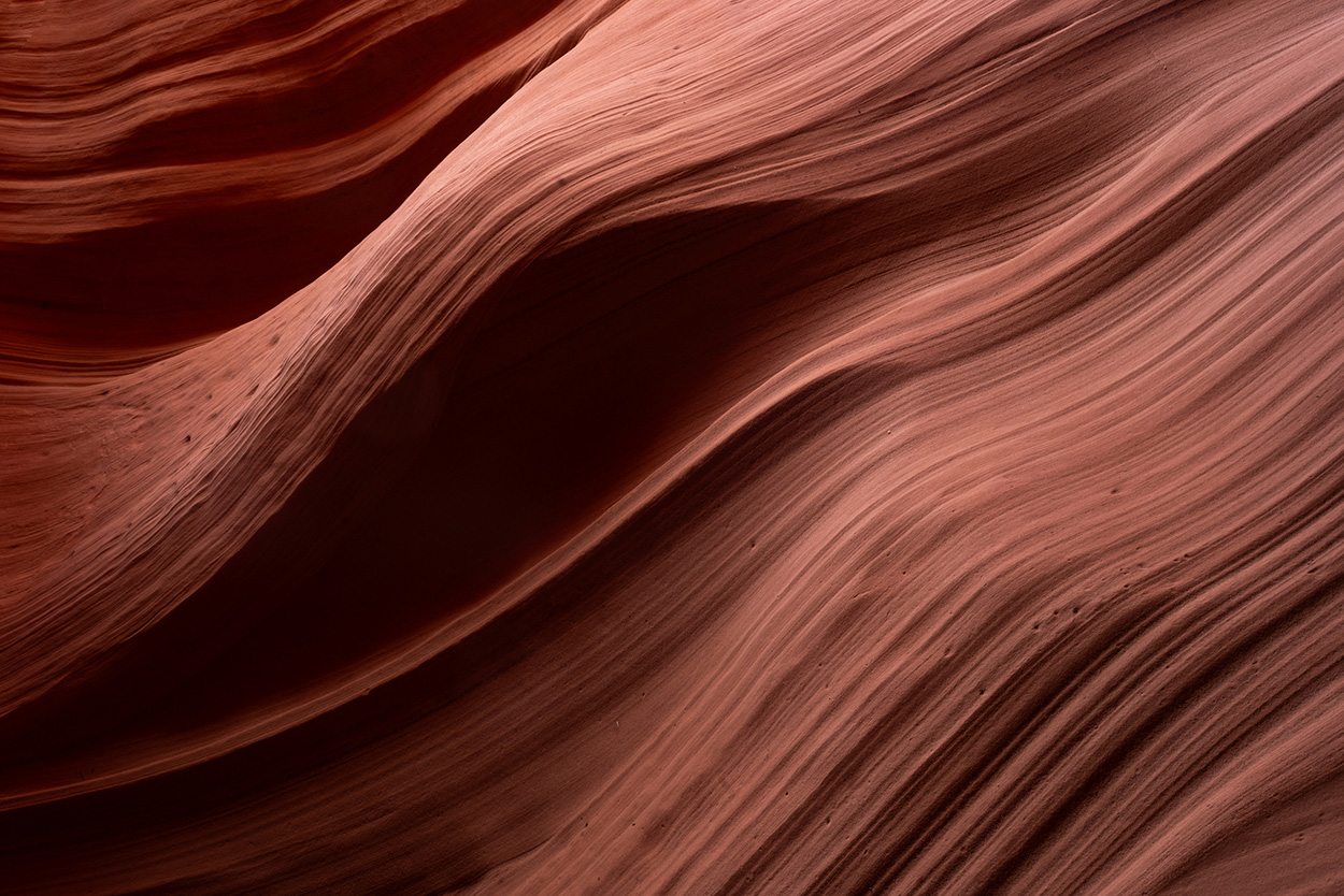 Close-up of smooth, wavy red sandstone layers, resembling flowing lines and textures, typical of geological formations.