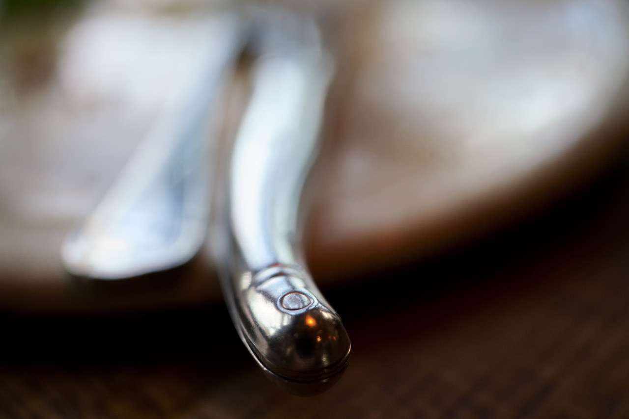 Nahaufnahme eines glänzenden Buttermessers und einer Gabel auf einer unscharfen Holzoberfläche, bei der die reflektierende Oberfläche des Metalls im Fokus steht.