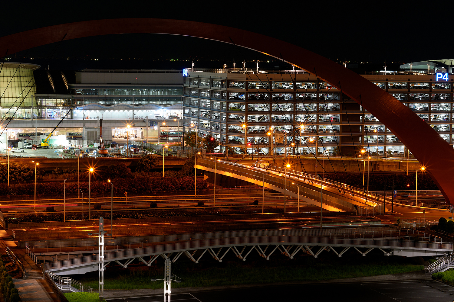 Night view of a brightly lit parking garage and building, with a striking arch and streets in the foreground.