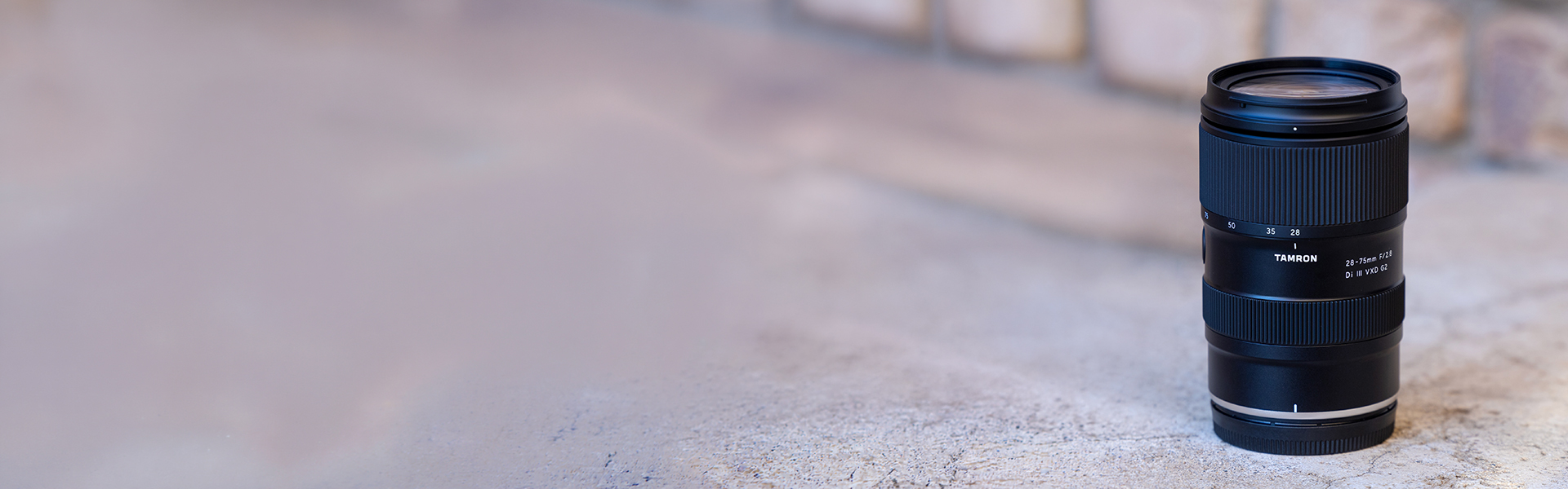 A camera lens stands upright on a textured, light grey surface with a blurred background.