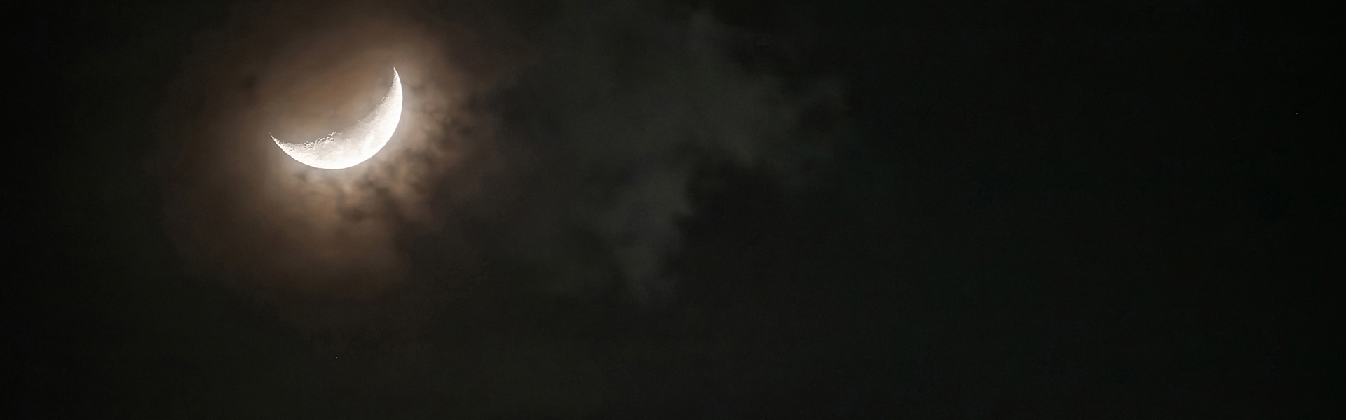 Crescent moon glowing softly in a dark, cloudy night sky.