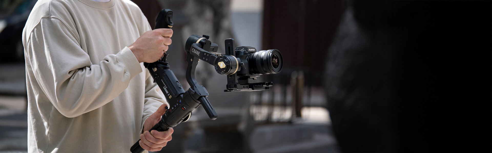 Person holding a camera mounted on a stabilizer, filming outdoors in a casual setting.