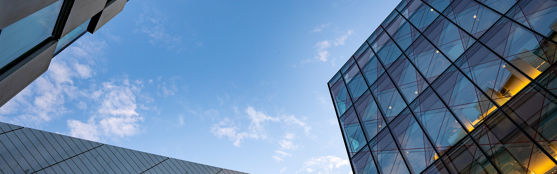 Moderne Gebäude aus Glas und Metall bilden vor dem Hintergrund eines blauen Himmels mit Wolken geometrische Winkel und unterstreichen so den architektonischen Kontrast und das Design.