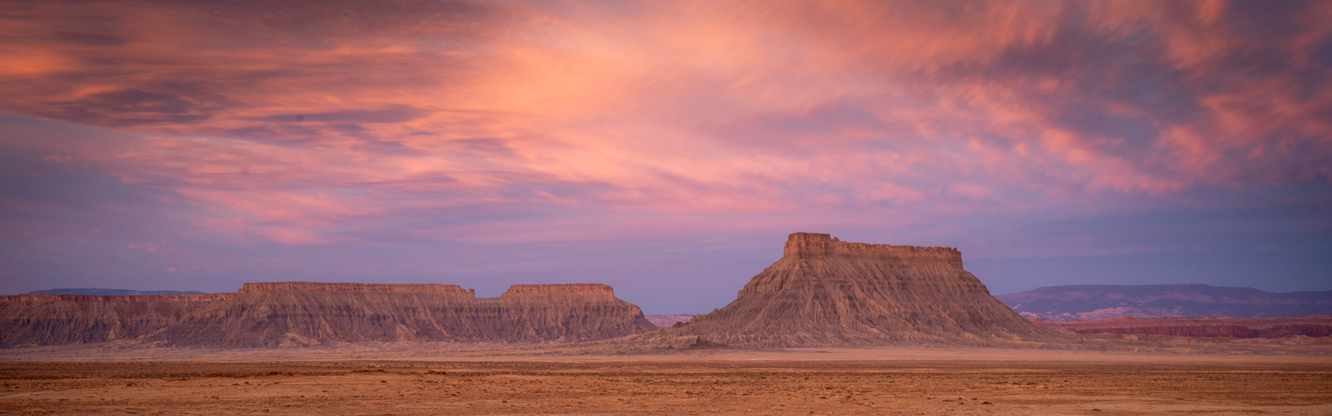 Desert landscape with flat mountains under a pink and purple sunset sky, creating a tranquil and expansive view.
