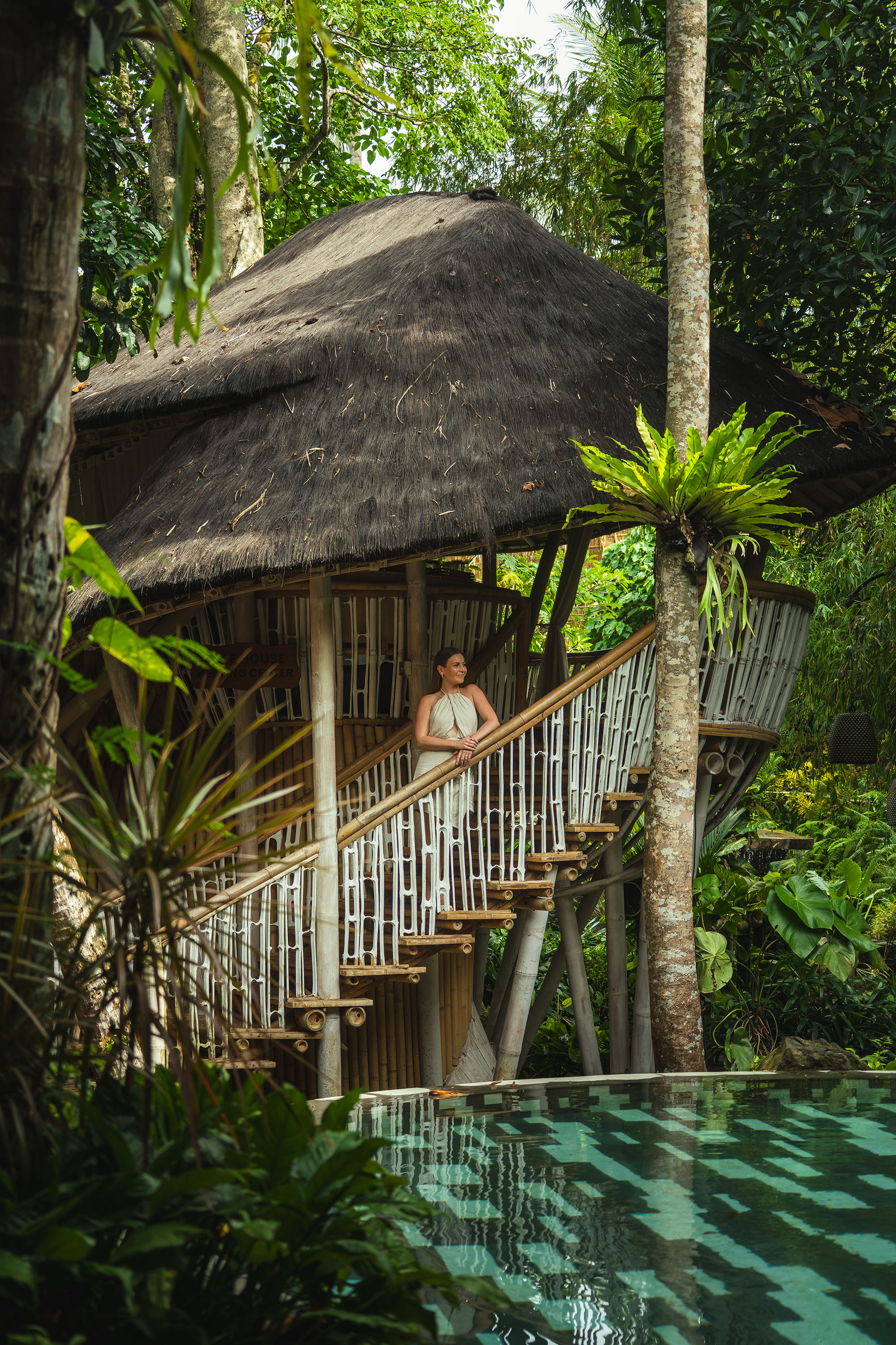 Ein Frau steht auf dem Balkon des Bamboo-Hauses umgeben von übrigem Grün