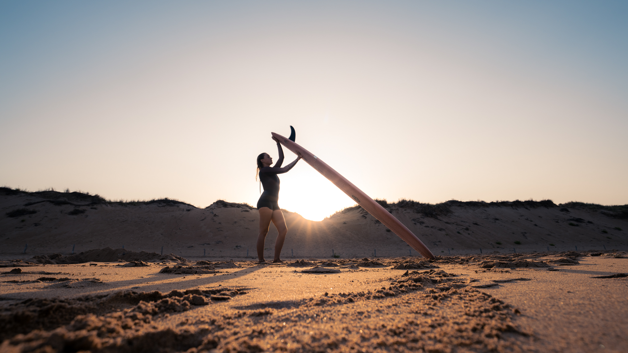 Aufnahme einer Surferin bei Gegenlicht am Strand.
