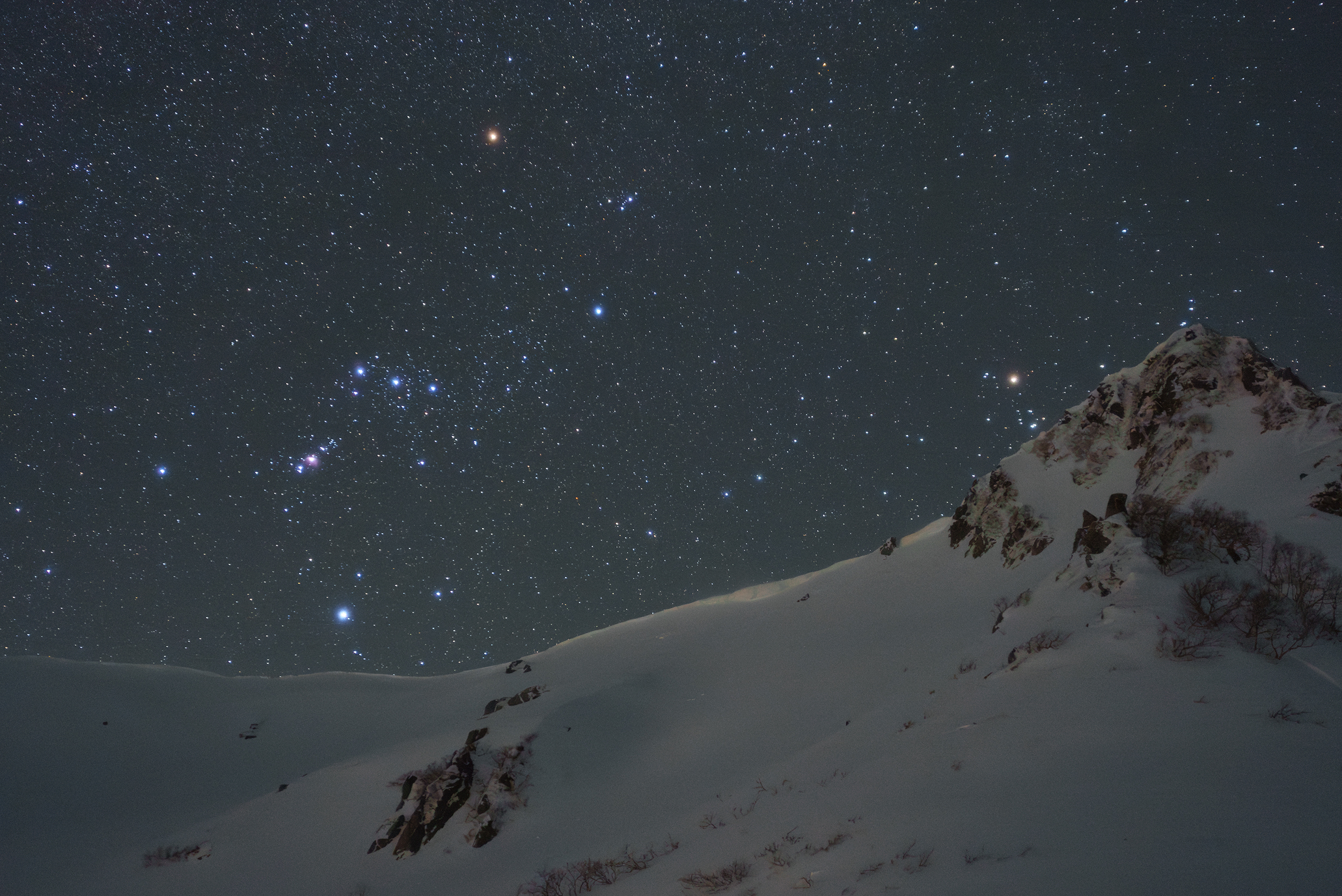 Gwieździste nocne niebo nad ośnieżonym górskim szczytem, z widocznymi konstelacjami i spokojną, ciemną atmosferą.