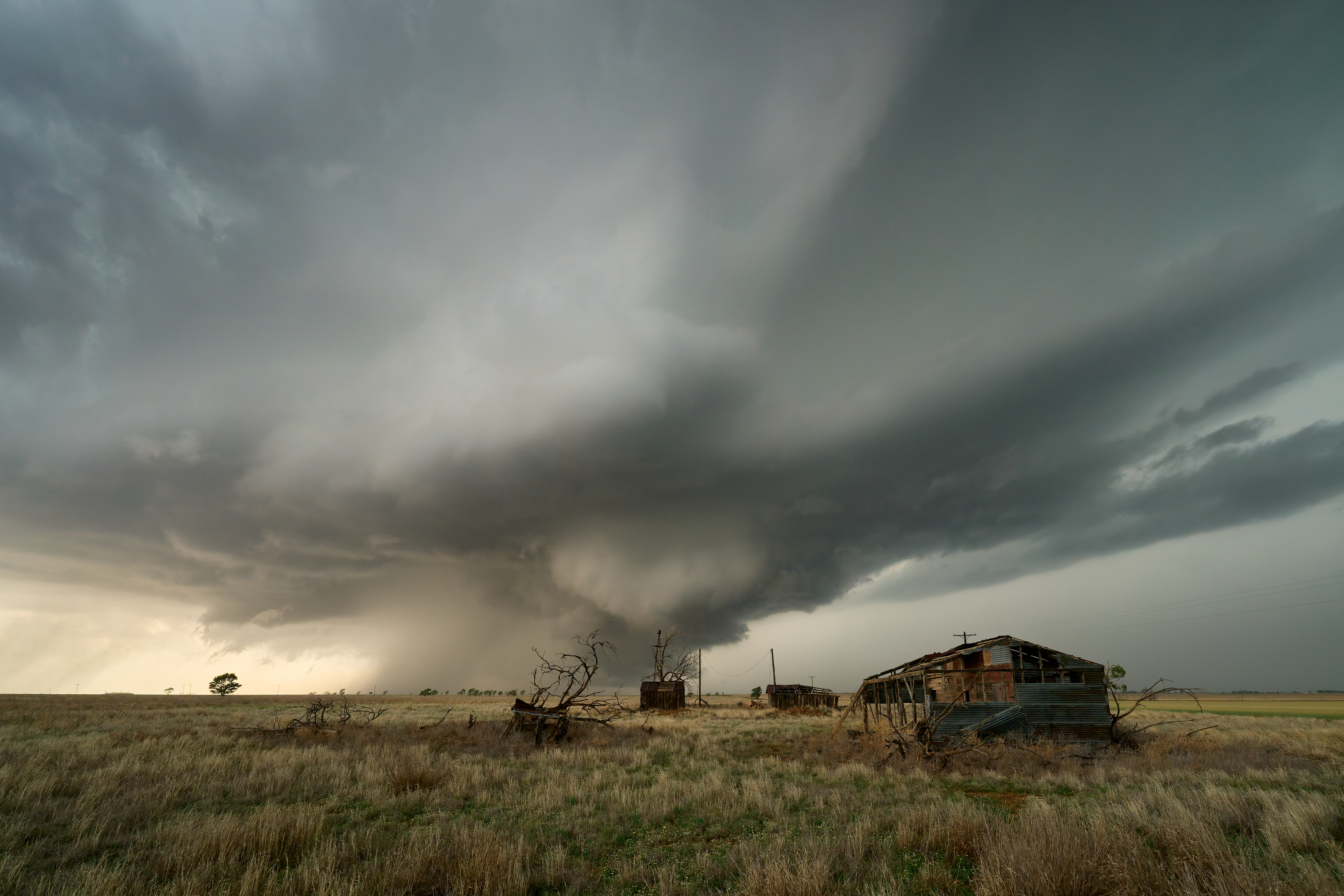 A vast landscape with a dramatic, swirling storm cloud overhead, an abandoned house, and barren trees in the foreground.