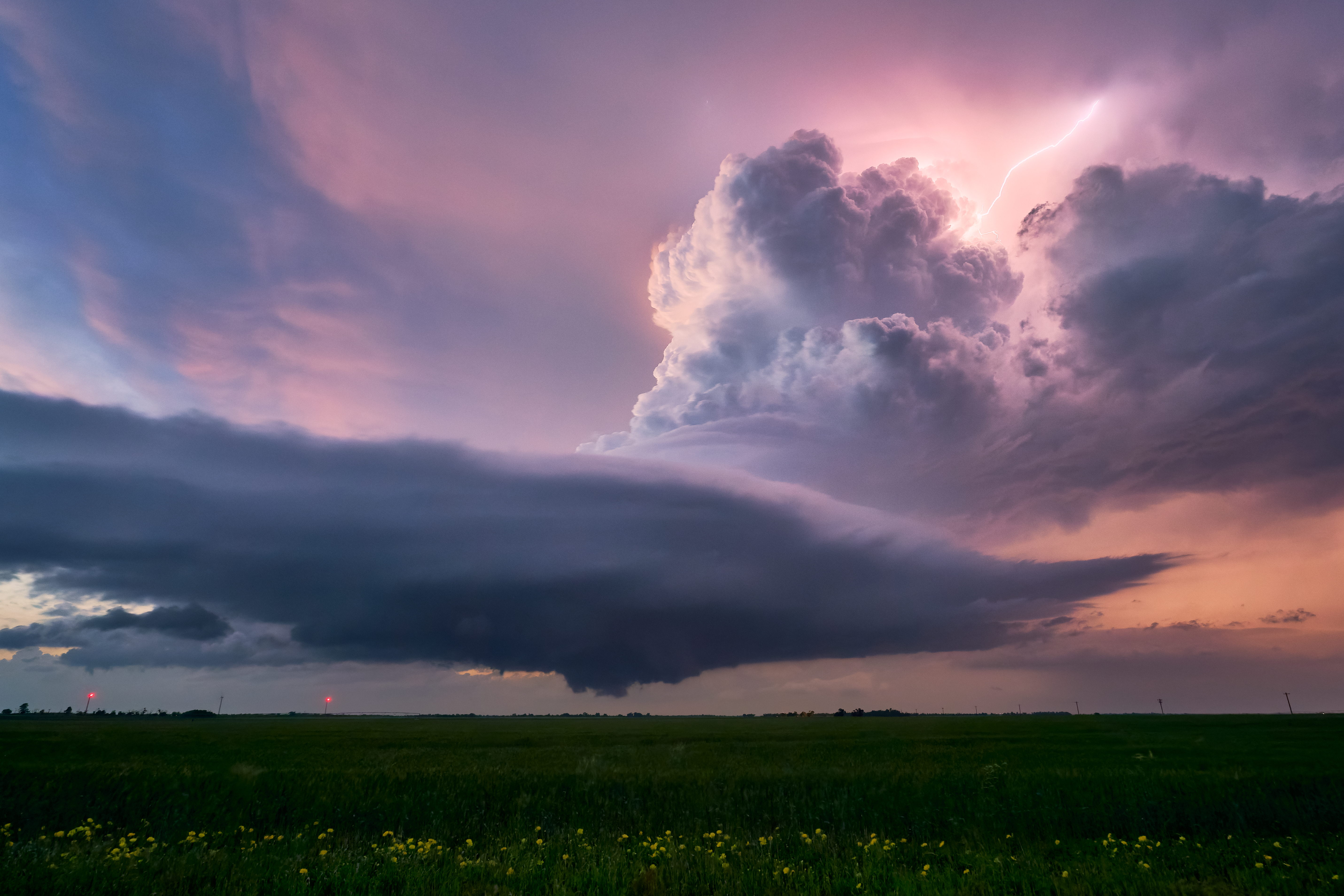 Dramatic sky with swirling storm clouds and a lightning bolt over a vast green field at sunset.