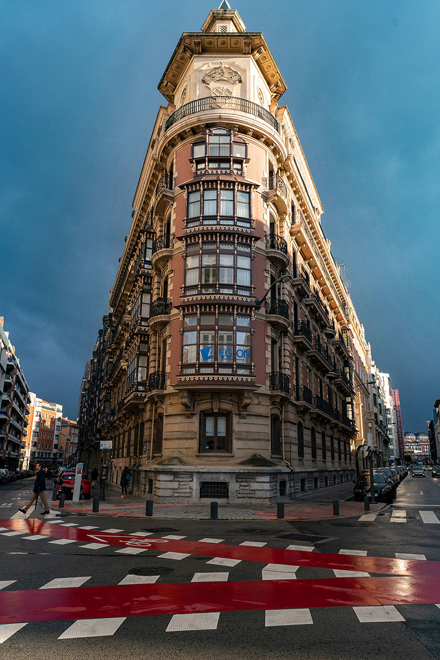 Ein hohes, prunkvolles Gebäude mit aufwendigen Details und Fenstern, das an einer Straßenkreuzung unter einem dramatischen Himmel steht.