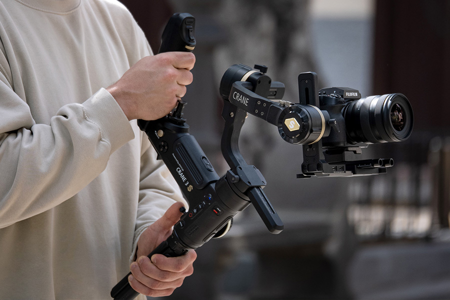 Eine Person hält eine Kamera, die auf einem Stabilisator montiert ist, und filmt draußen in entspannter Umgebung.