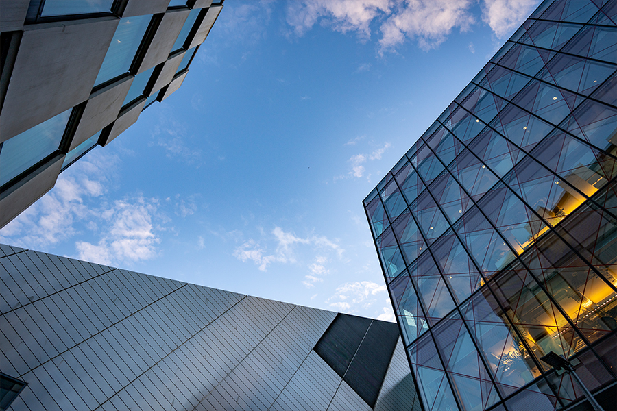 Moderne Gebäude aus Glas und Metall bilden vor dem Hintergrund eines blauen Himmels mit Wolken geometrische Winkel und unterstreichen so den architektonischen Kontrast und das Design.