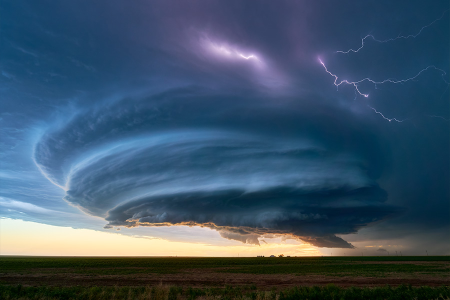 Dramatisches Superzellen-Gewitter mit rotierender Wolkenformation und Blitzen am Himmel über einer flachen Landschaft in der Abenddämmerung.