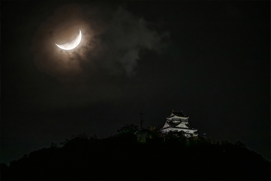 Media luna iluminando el cielo oscuro, con la silueta de una pagoda sobre una colina rodeada de nubes.