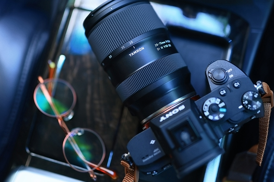 A camera with a large lens and wire-framed sunglasses sit on a car console with visible gear shift and buttons.