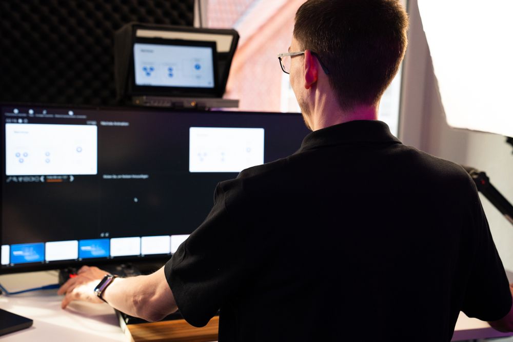 Person bei der Arbeit an einem Videoproduktionsplatz mit mehreren Monitoren