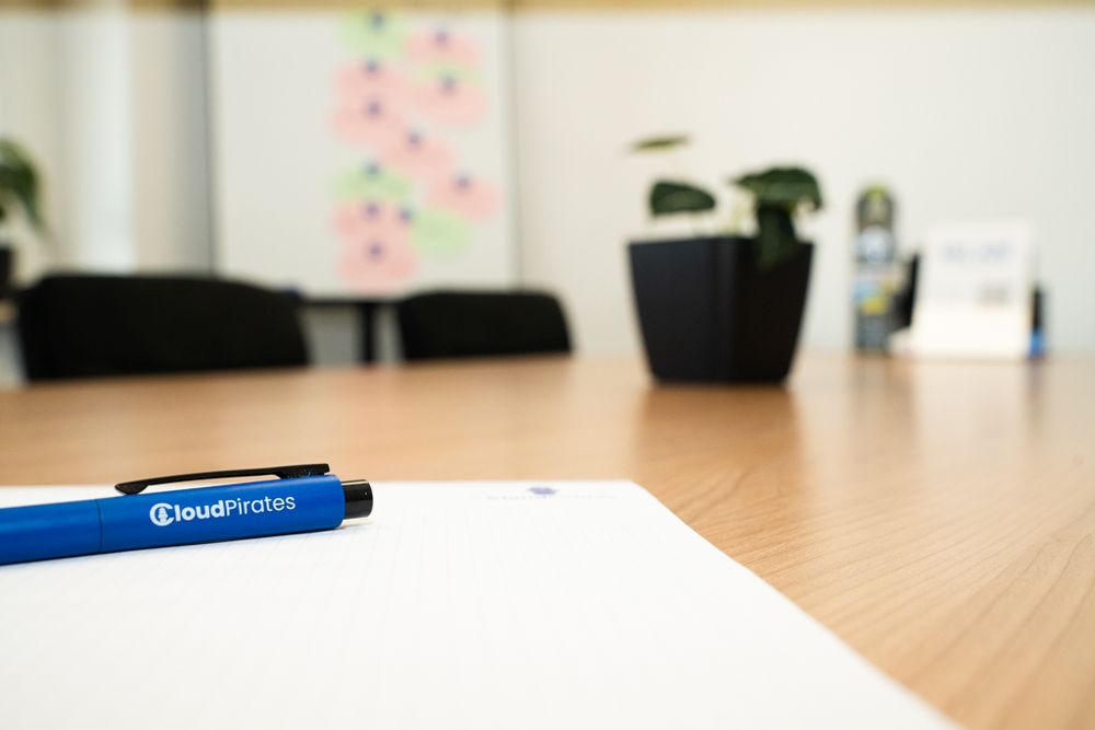 Konferenztisch mit CloudPirates-Kugelschreiber, Papier und Pflanze