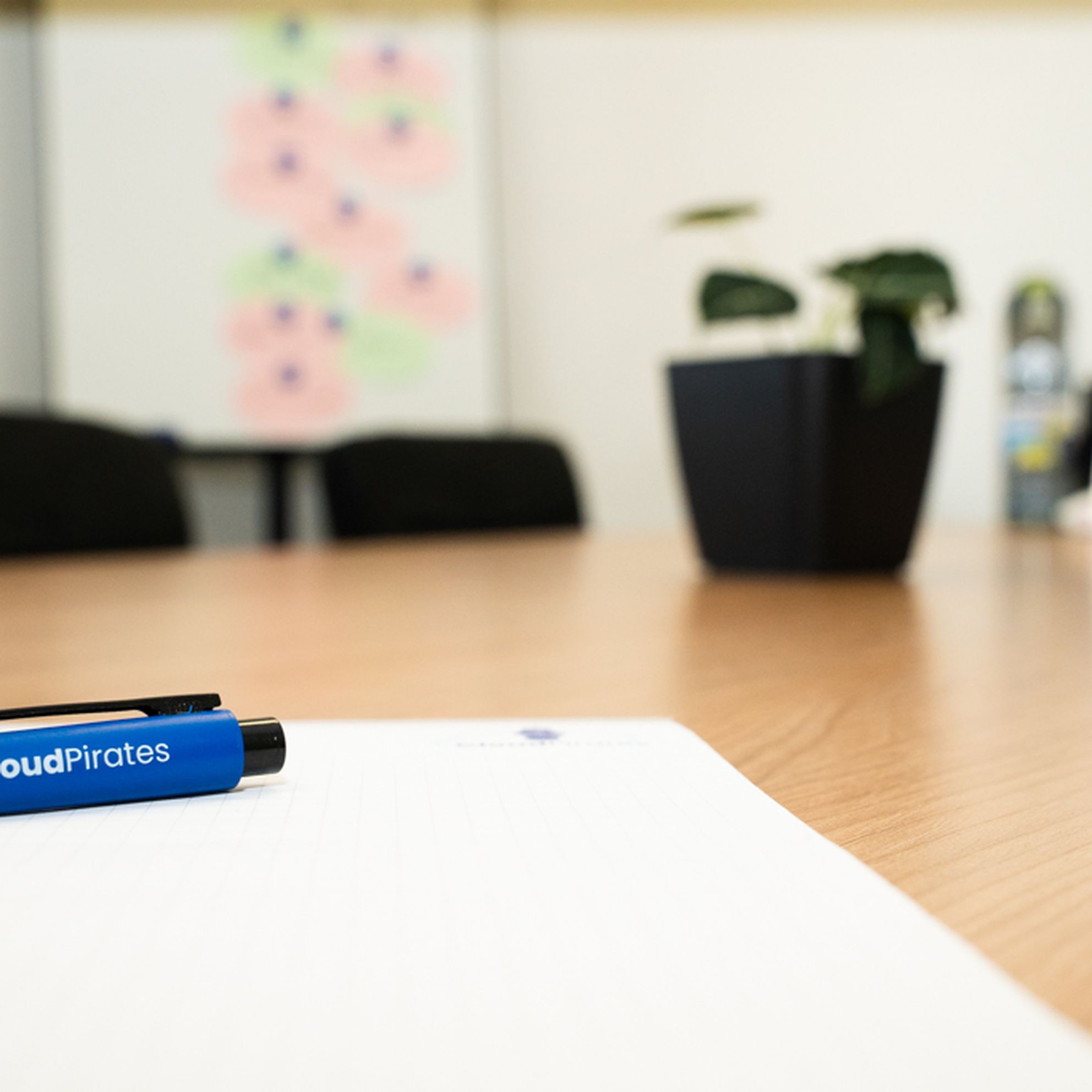 Konferenztisch mit CloudPirates-Kugelschreiber, Papier und Pflanze