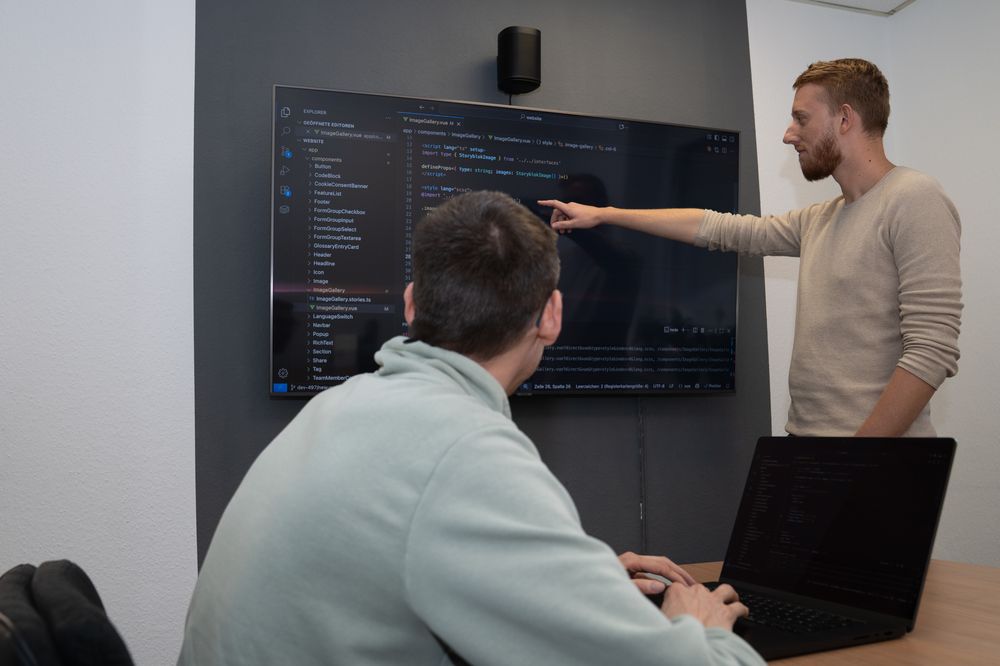 Dennis (left) and Dominik (right) are reviewing code displayed on a TV screen.