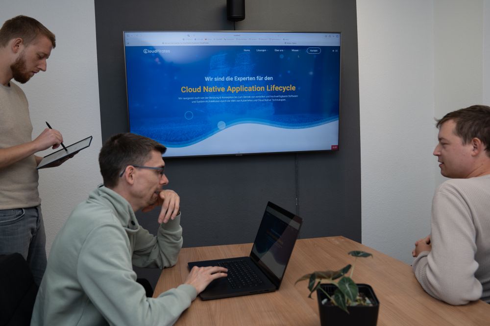 Dominik (left, with paper tablet), Dennis (middle, with laptop) and Yannick (right) are reviewing changes to our website displayed on a TV screen.