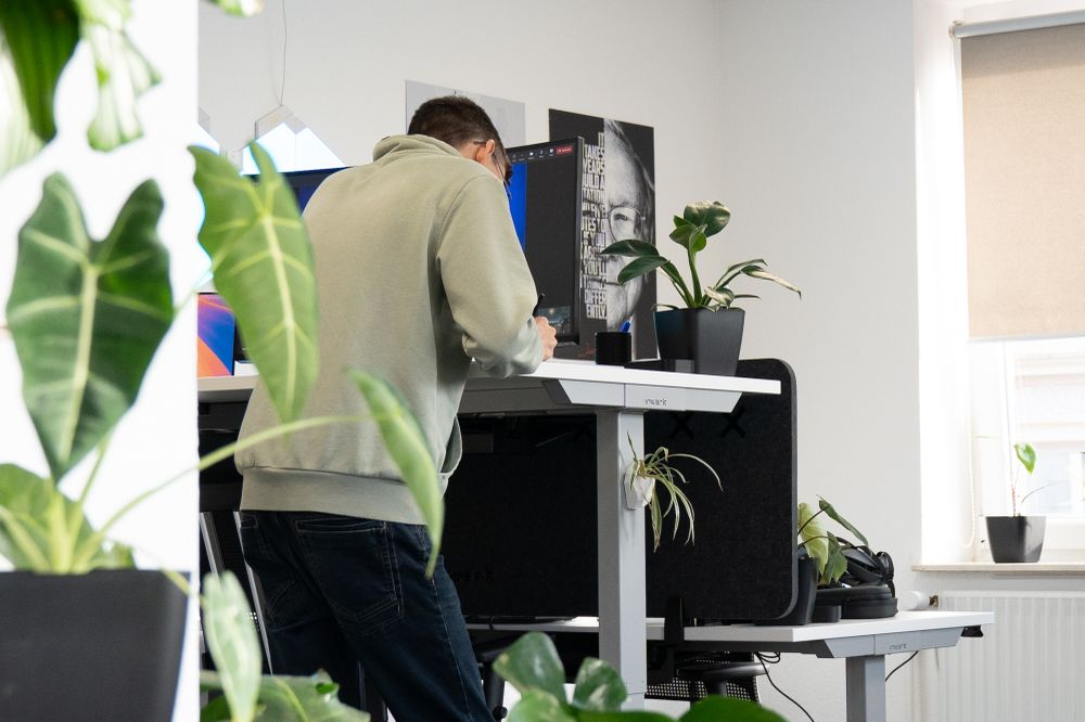 Dennis is standing at his height-adjustable worksplace. A lot of plants are around.