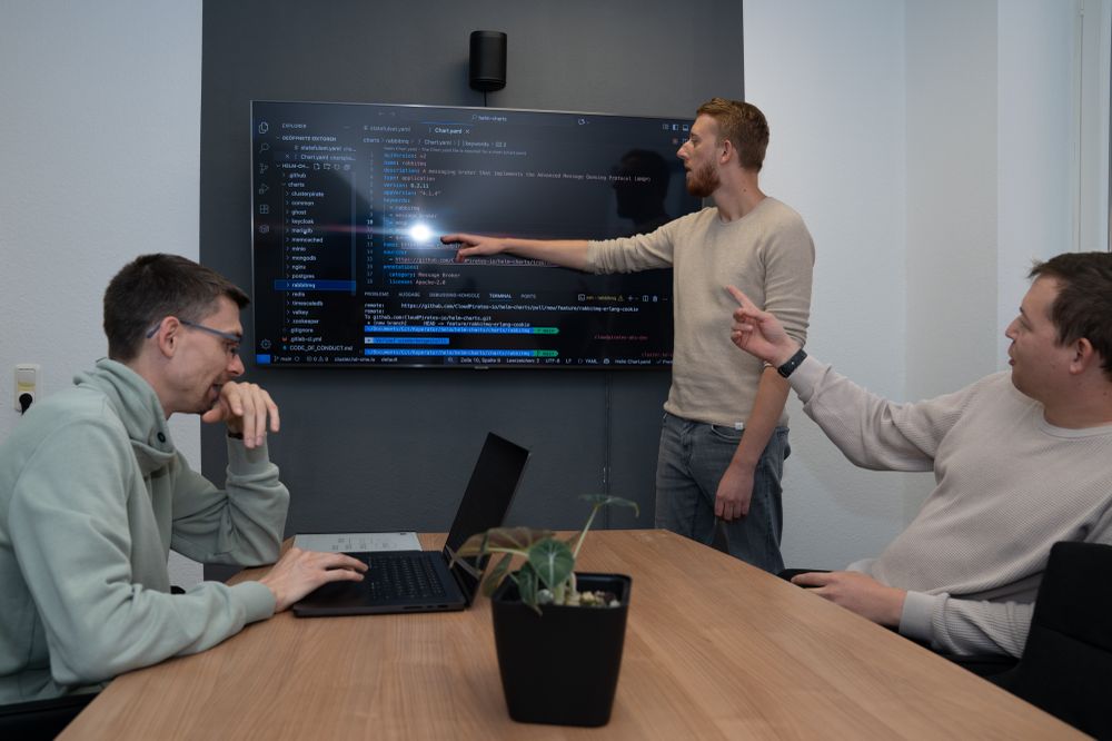 Dennis (left), Dominik (middle) and Yannick (right) are reviewing code displayed on a TV screen.