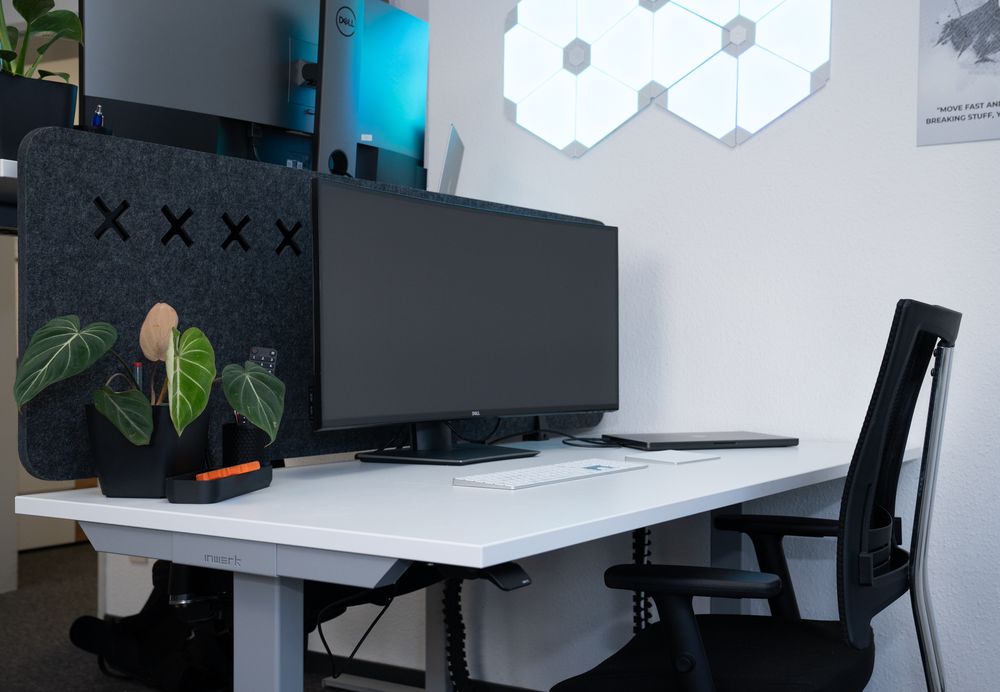 One of our workplaces: a height-adjustable table with an ergonomic chair, a wide-screen monitor, a keyboard with a trackpad and a closed laptop.