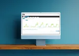 A computer monitor displaying a line graph with fluctuating data, set on a wooden shelf against a blue wall.