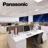 Modern office space with cubicles, computers, and a city skyline view at night. The Panasonic logo is in the top left corner.