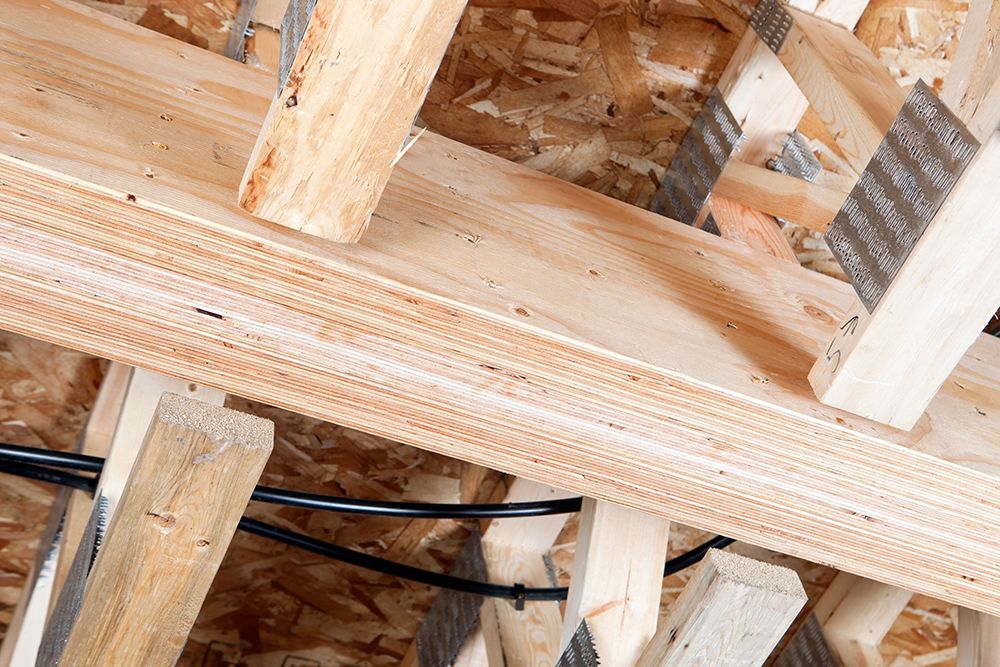 Wooden ceiling framework with beams and metal connectors, showcasing construction details and layered plywood.