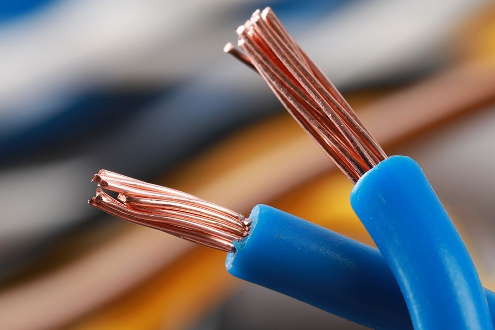 Close-up of two blue insulated copper wires with exposed strands, set against a blurred multicolored background.