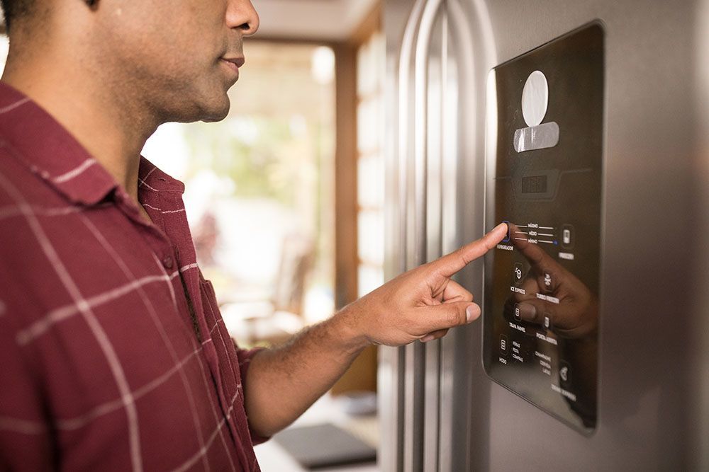 A person in a red plaid shirt presses a button on a refrigerator's digital display panel.