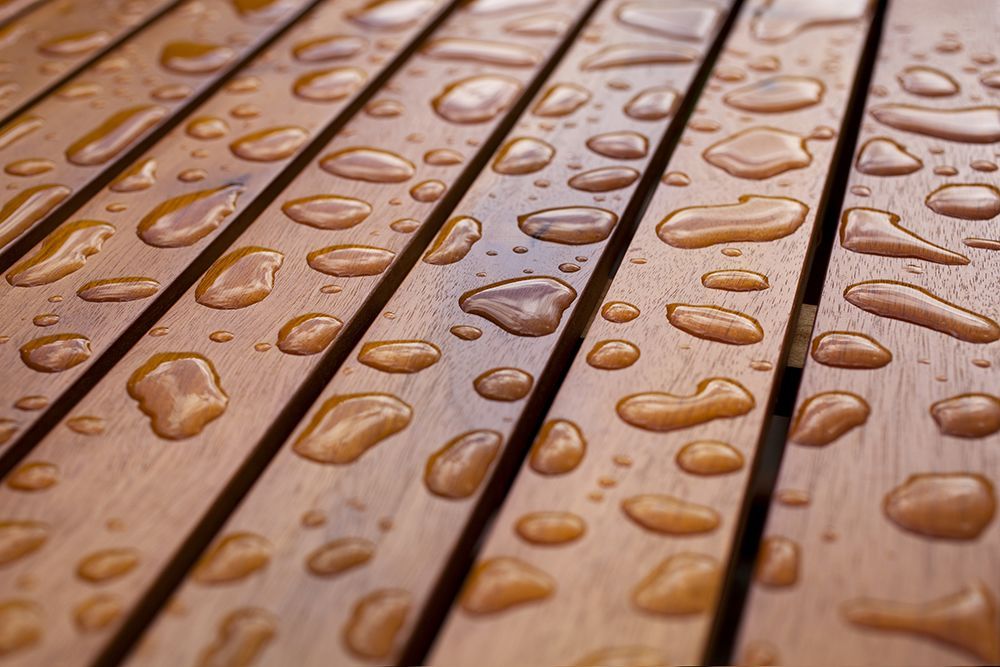Close-up of rain droplets on a wooden surface, highlighting the texture of the wood and the glossiness of the water drops.