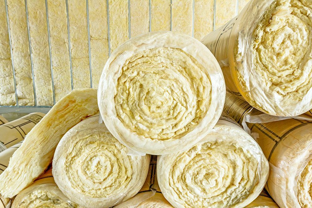 Rolls of yellow insulation material stacked vertically and horizontally in a storage area.