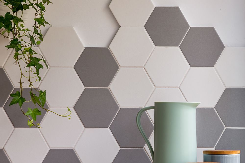 Hexagonal wall tiles in white and gray with a green ivy plant hanging. Below is a mint green jug and a small container with a wooden lid.