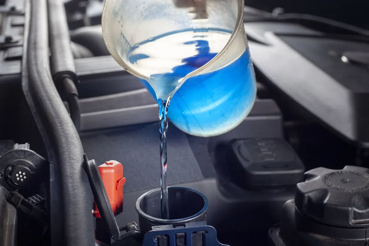 Pouring blue antifreeze into a car engine's coolant reservoir.