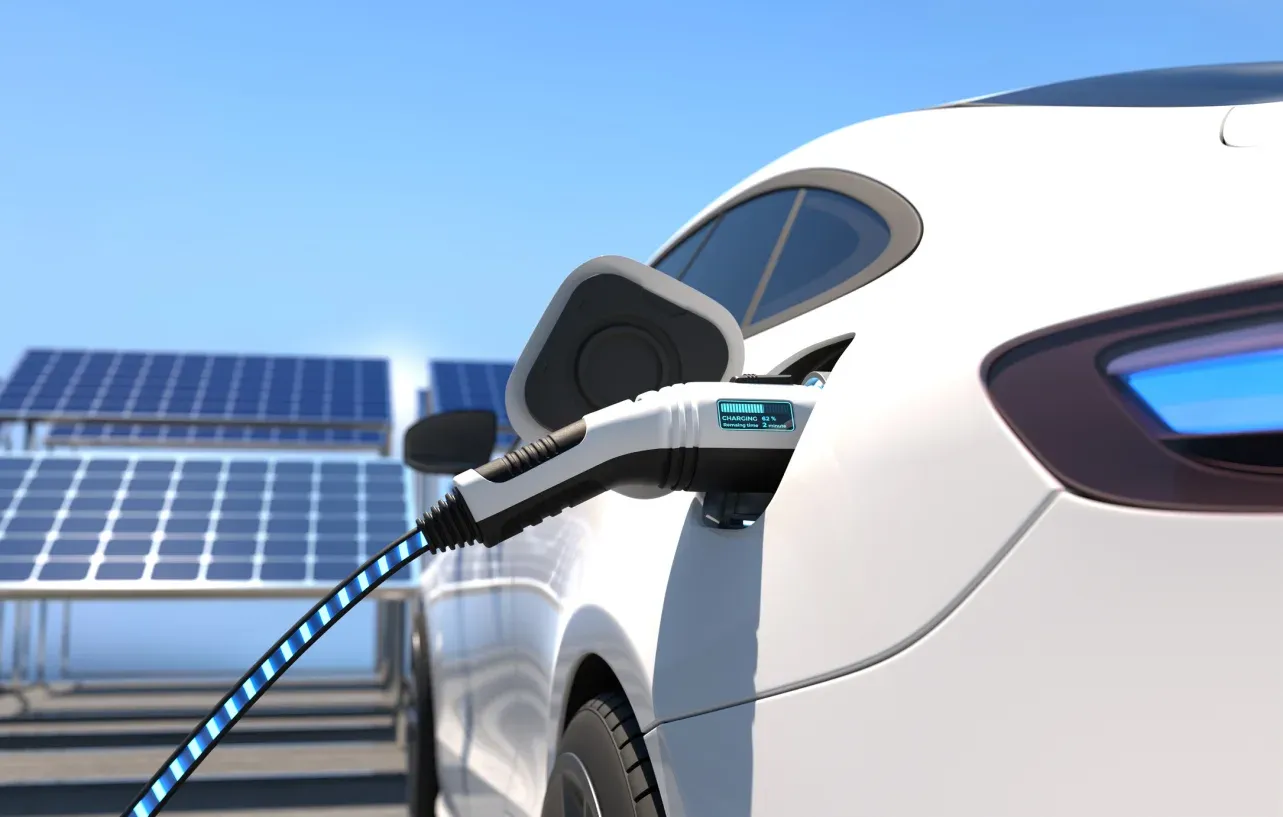 Electric car charging with a cable, surrounded by solar panels under a clear blue sky.