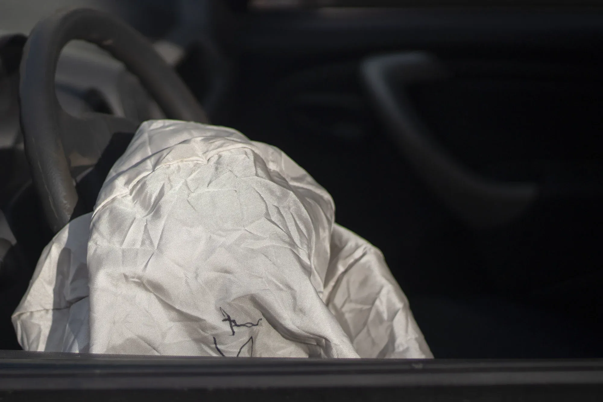Deployed car airbag in front of a steering wheel inside a vehicle.