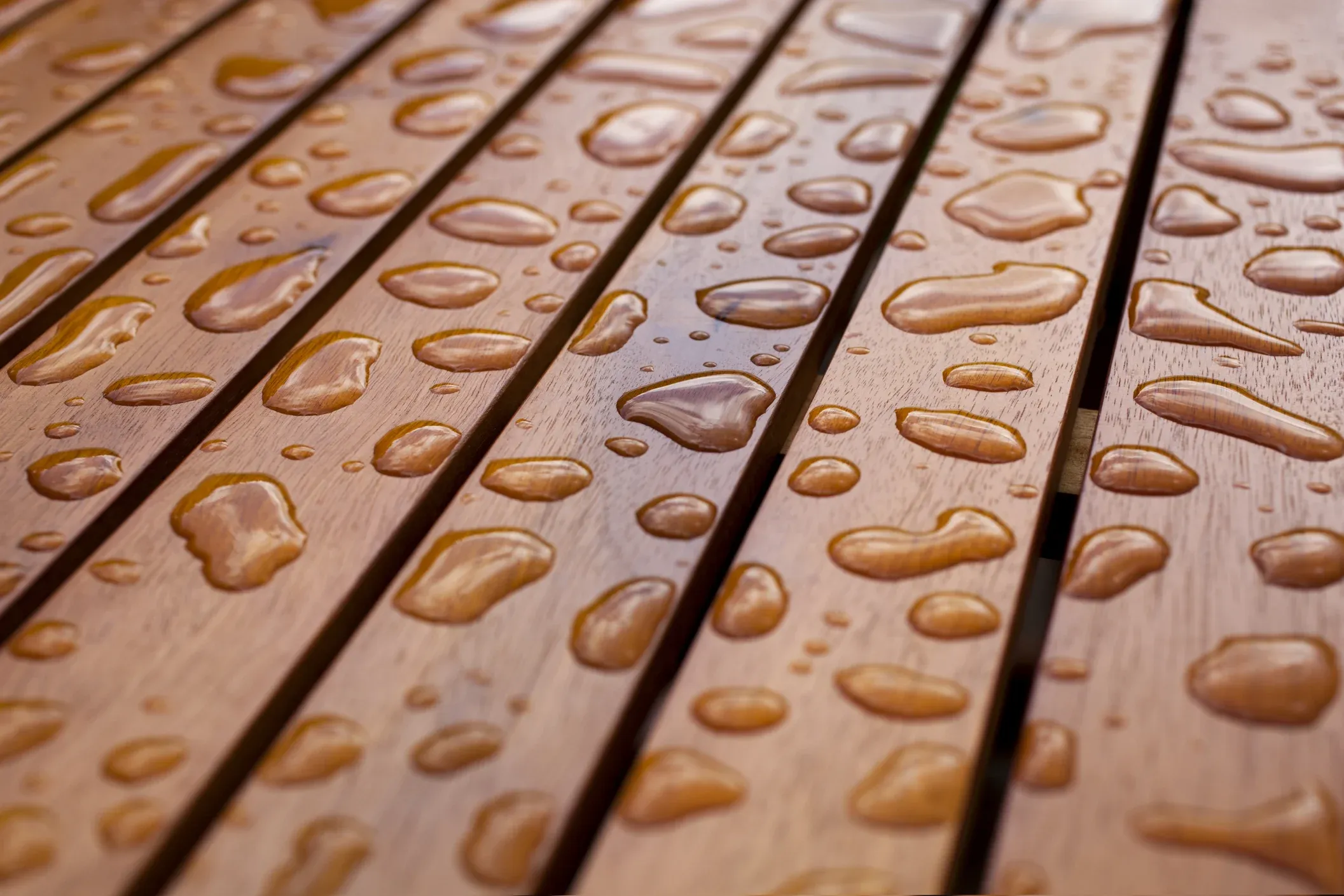 Close-up of water droplets scattered across a smooth, wooden surface, creating a glossy effect on the rich brown wood.