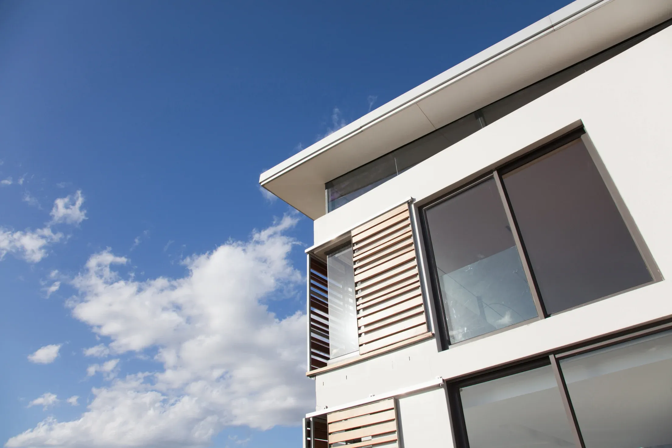 Modern building with large windows and wooden slats against a clear blue sky with scattered clouds.