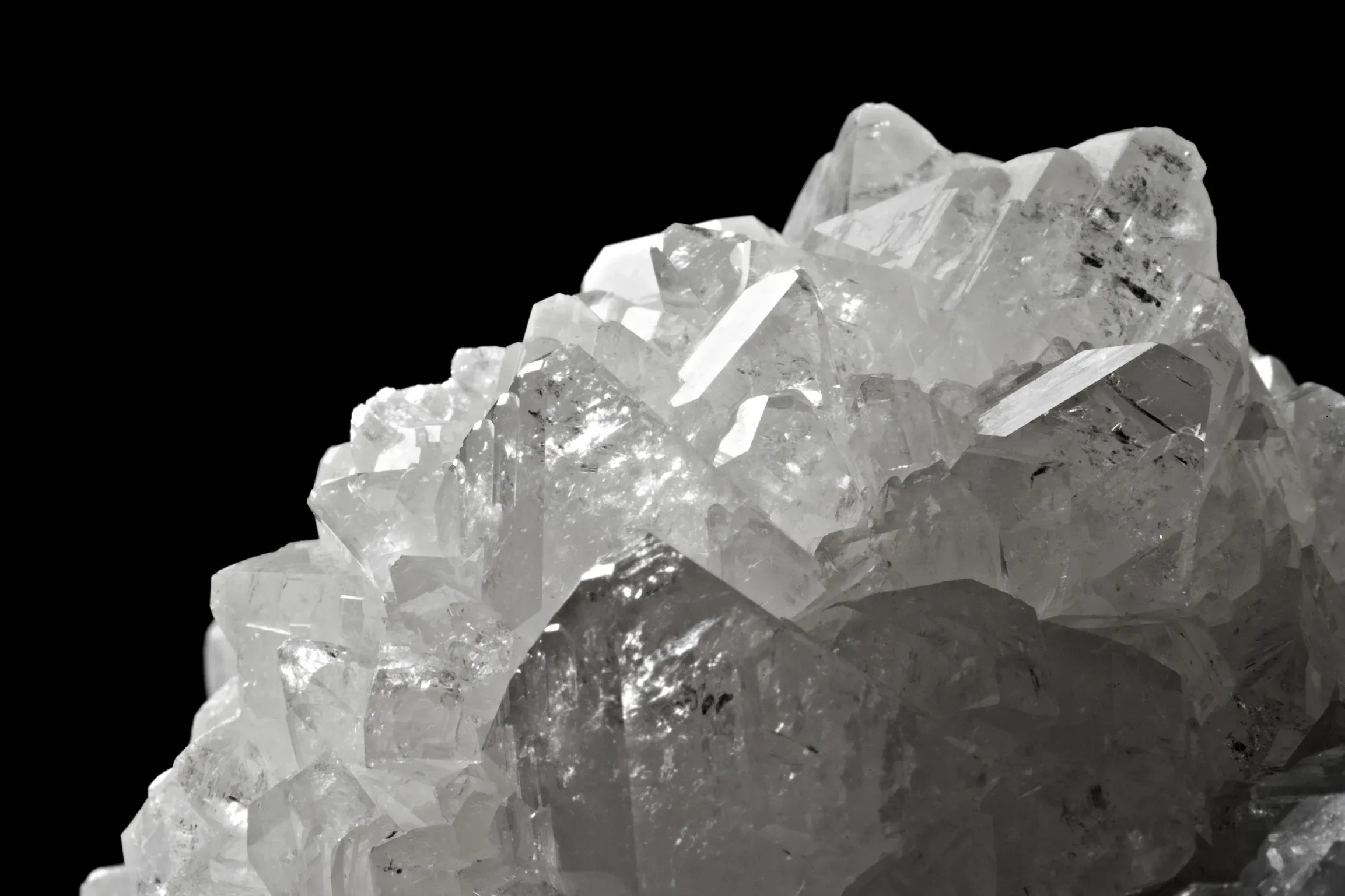 Cluster of clear quartz crystals with sharp angles and shiny surfaces set against a black background.