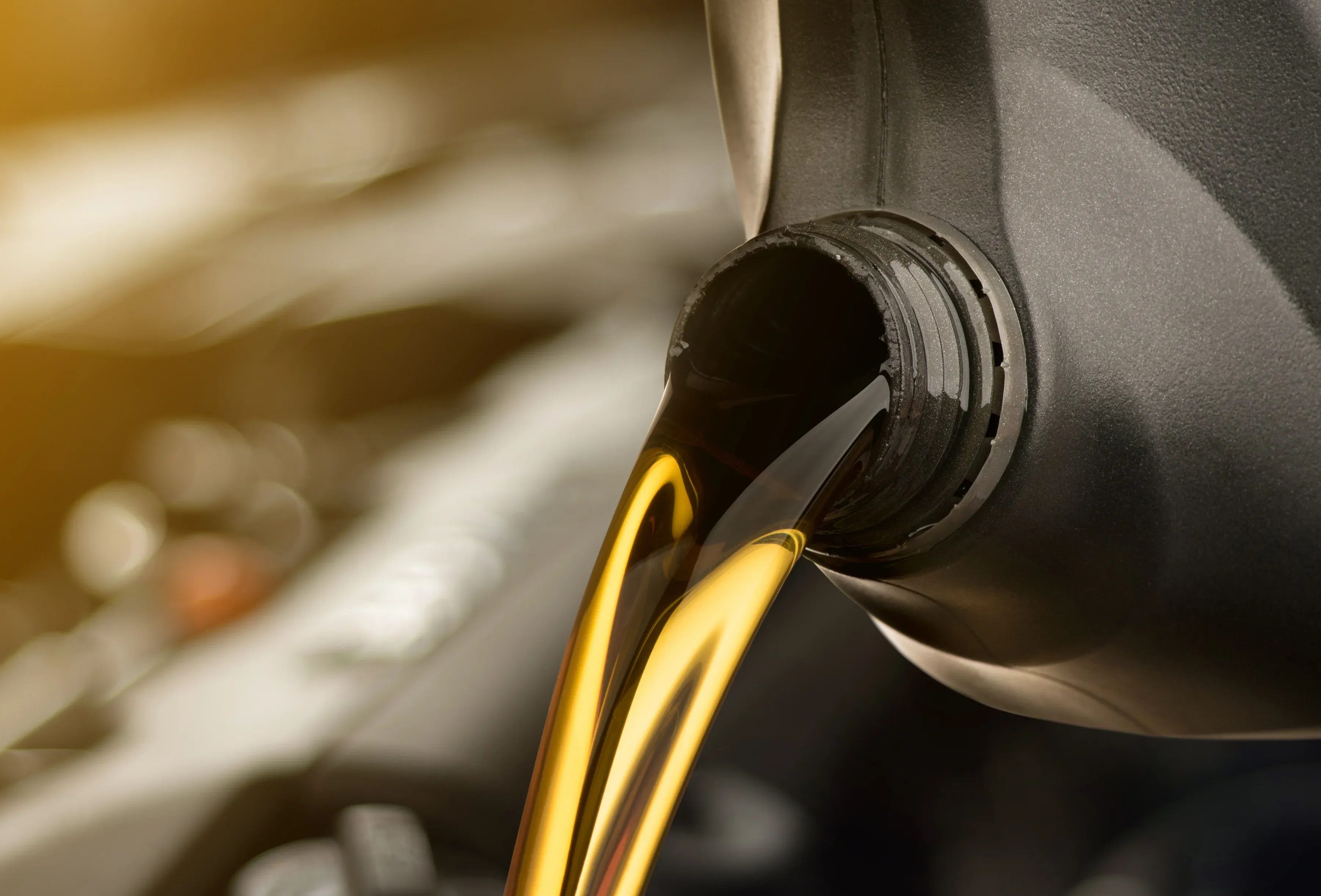 Pouring golden motor oil from a dark container into an engine, with a blurred background.