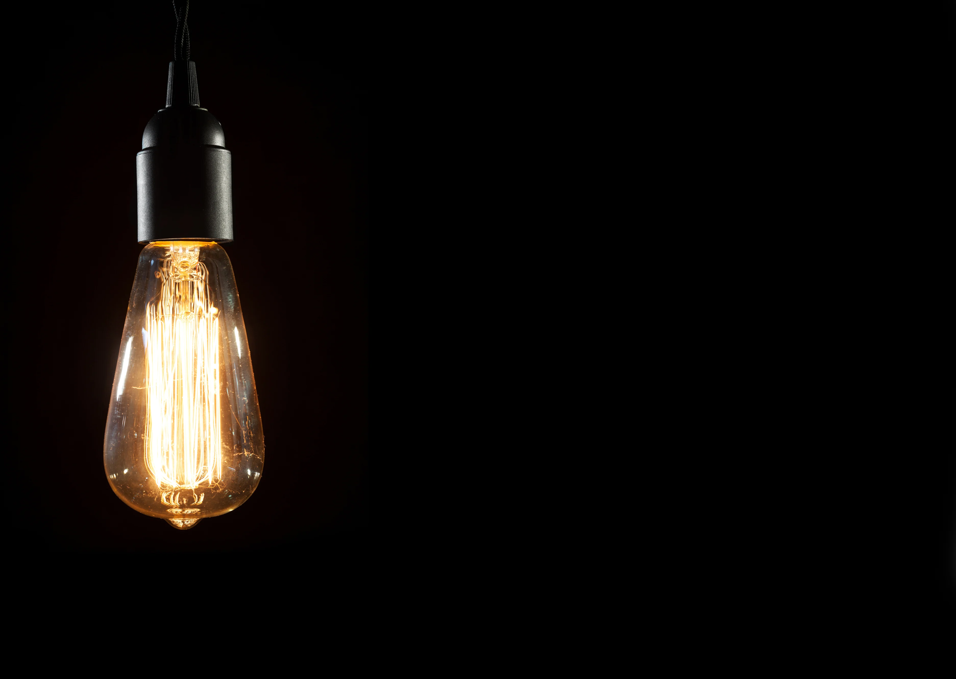 A glowing vintage Edison bulb hangs in the dark, showcasing its intricate filament and warm light.