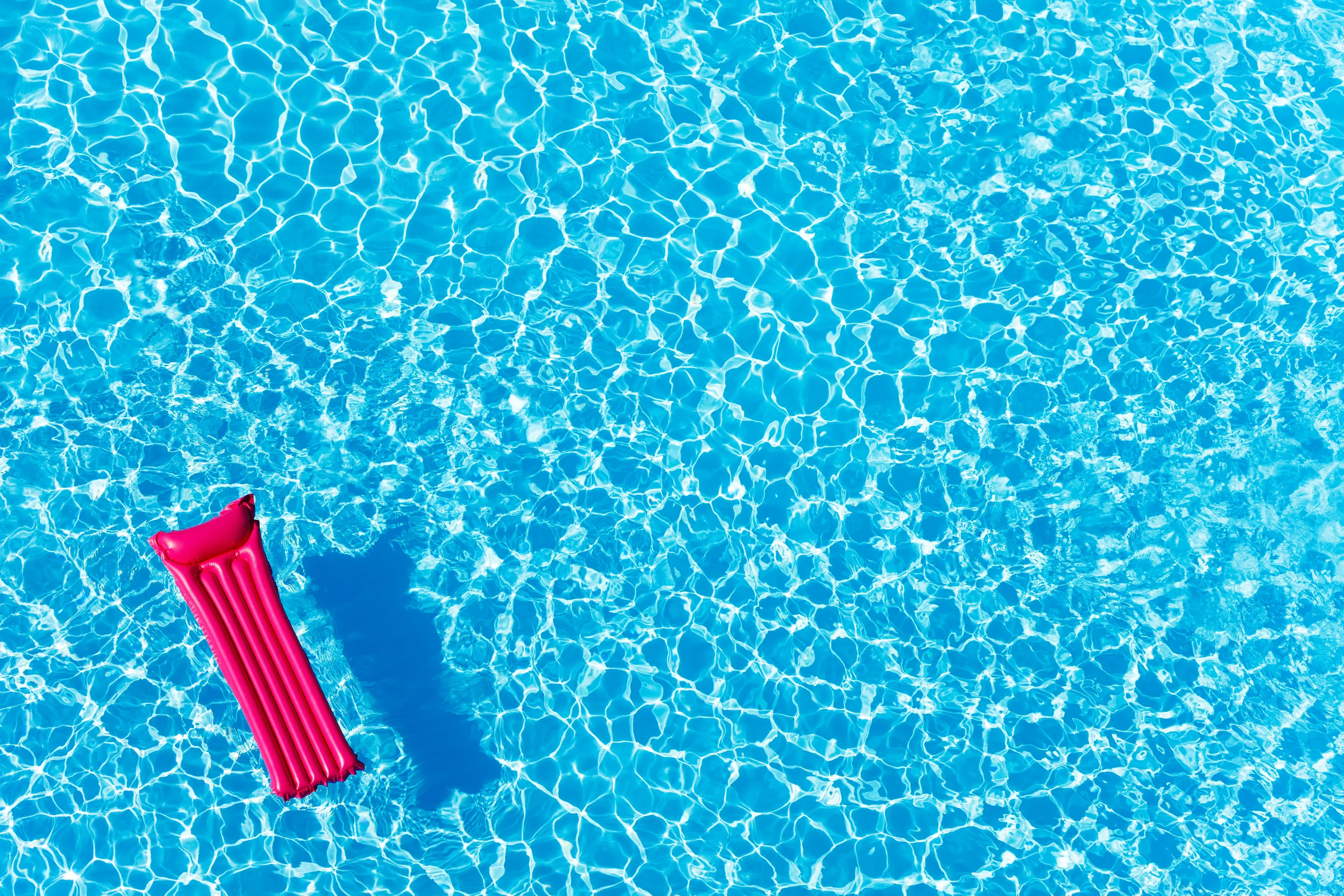 A bright pink inflatable float drifts in a clear blue swimming pool, with sunlight creating patterns on the water's surface.