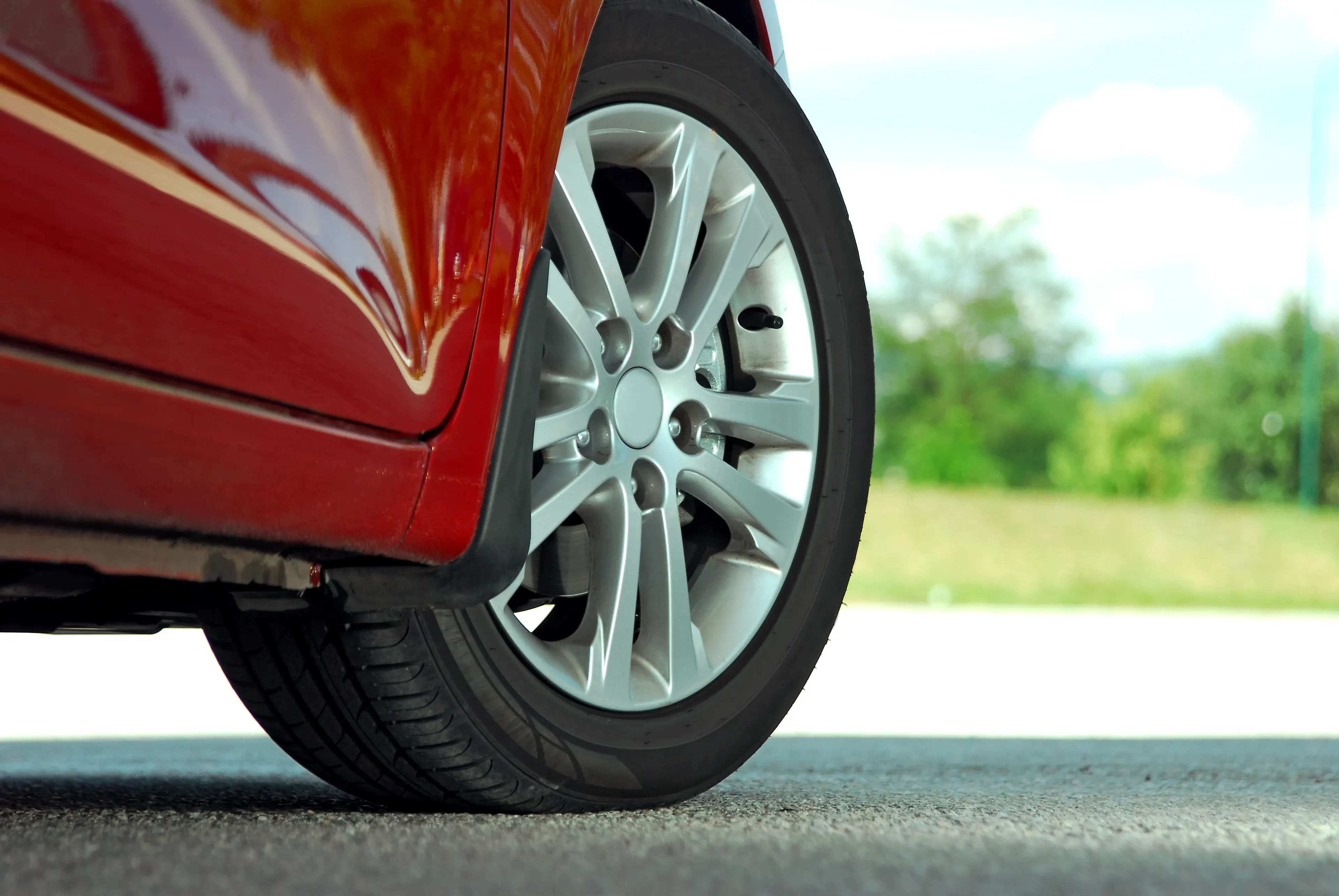 Close-up of a silver car wheel and tire on a red vehicle, parked outdoors on a sunny day.