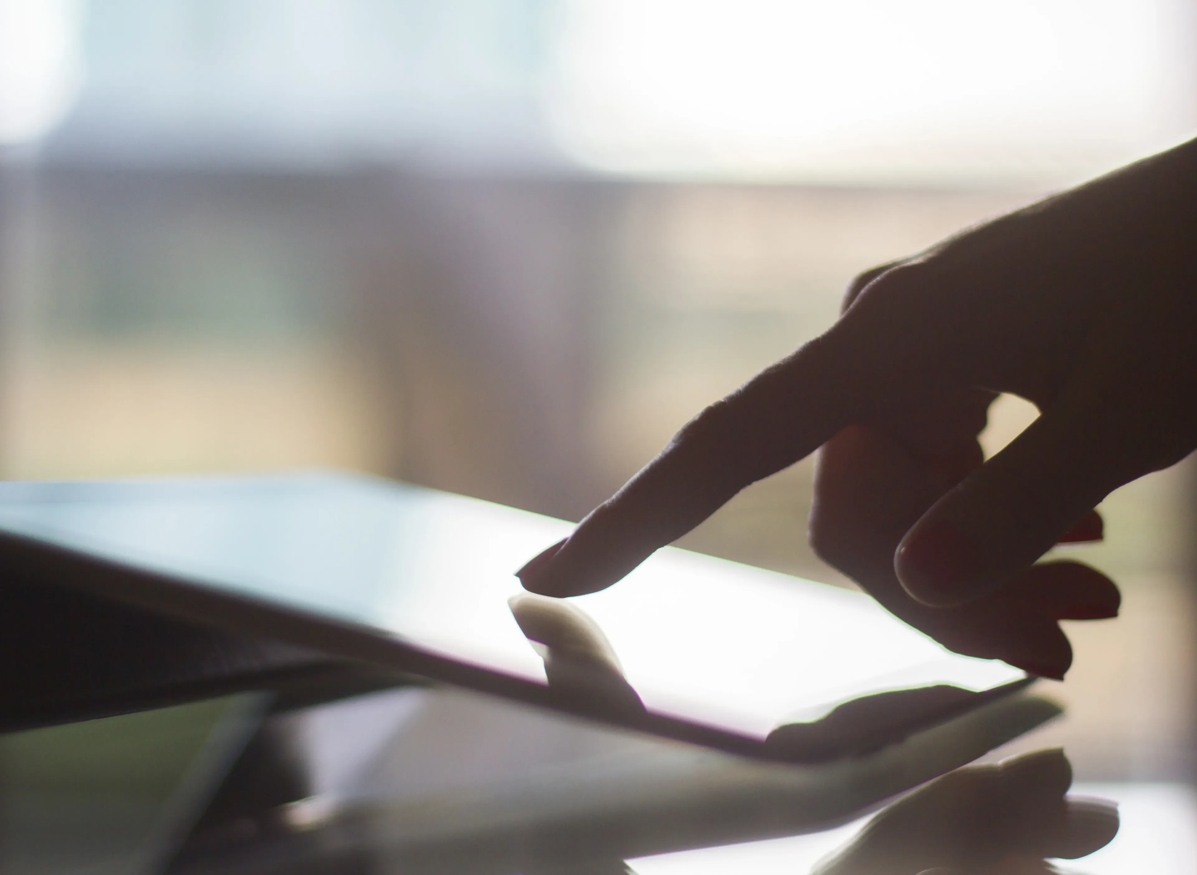 Finger touching a lit tablet screen in a dimly lit environment.