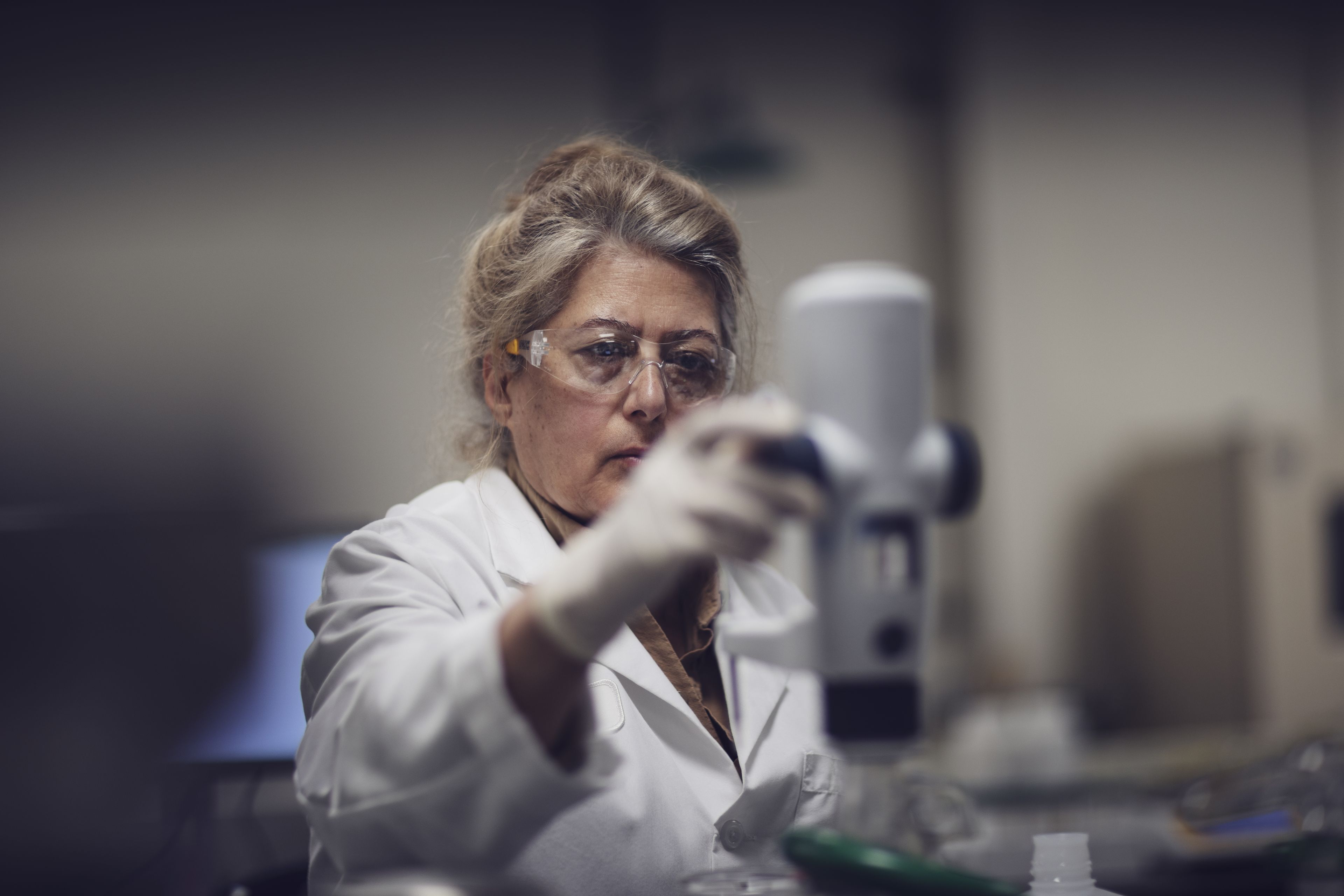 A scientist wearing safety goggles and gloves operates laboratory equipment, focused intently on her work.